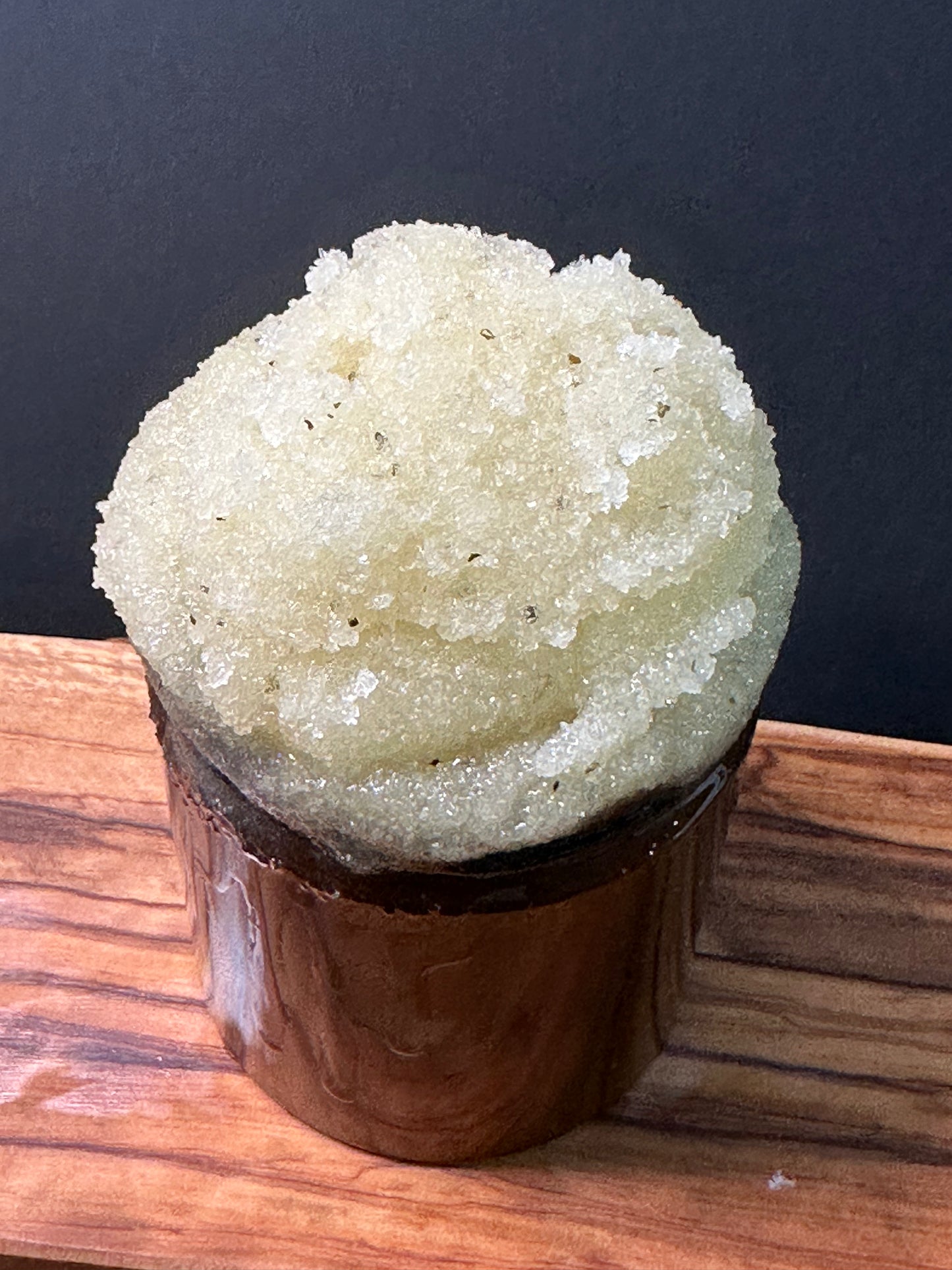 Amber plastic jar filled and topped with fine white sugar thick, pale golden crystalline layer, set on a wooden surface against a dark background