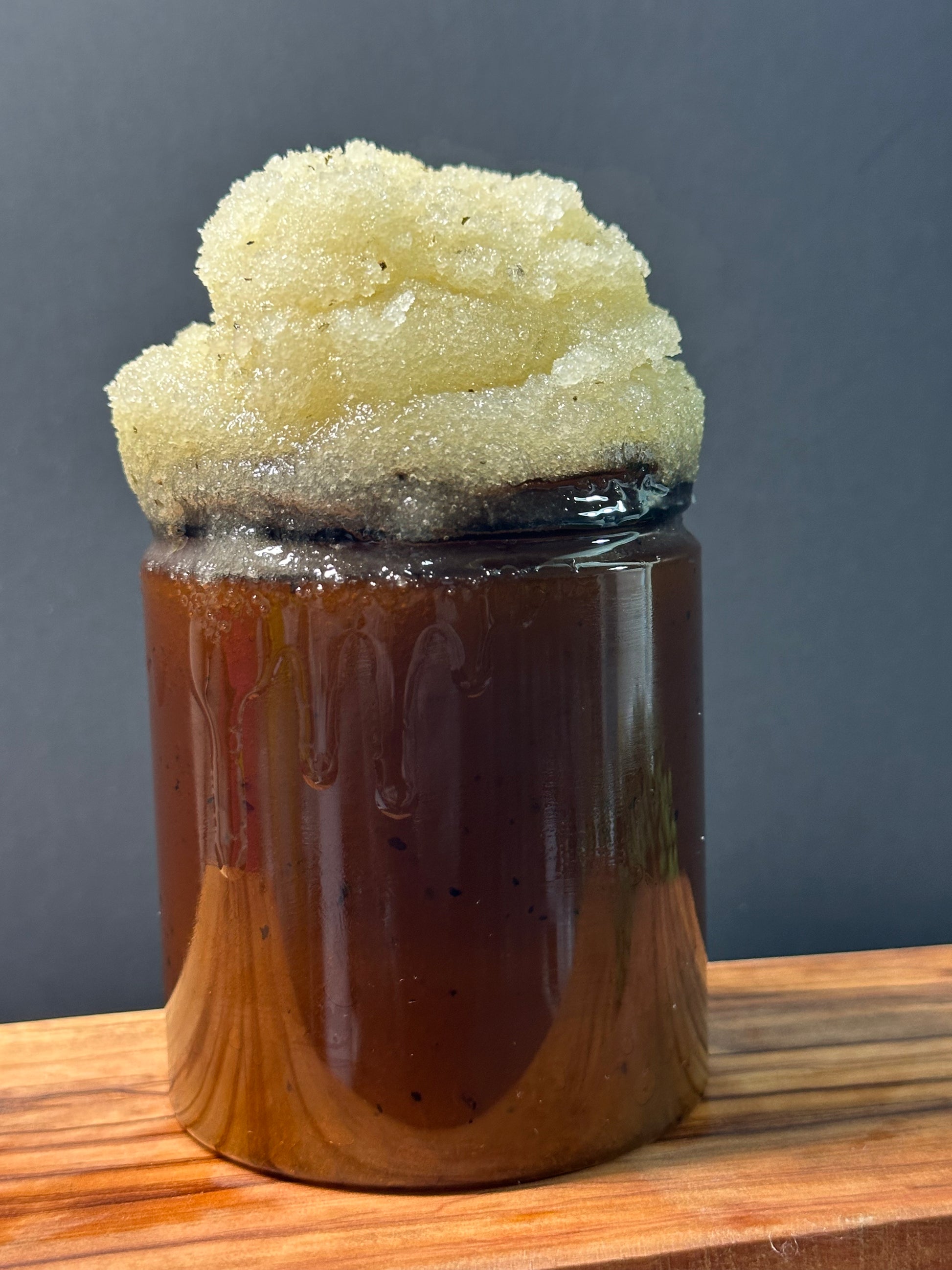 Amber plastic jar filled and topped with fine white sugar thick, pale golden crystalline layer, set on a wooden surface against a dark background 
